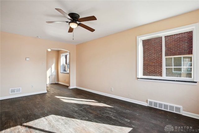 spare room featuring wood finished floors, arched walkways, visible vents, and baseboards