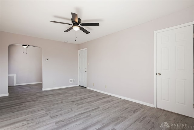 unfurnished room featuring wood finished floors, visible vents, baseboards, arched walkways, and ceiling fan