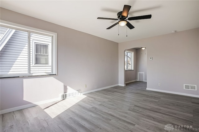 spare room with visible vents, arched walkways, baseboards, and wood finished floors