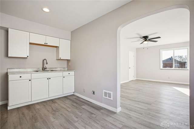 kitchen featuring visible vents, baseboards, arched walkways, white cabinetry, and a sink