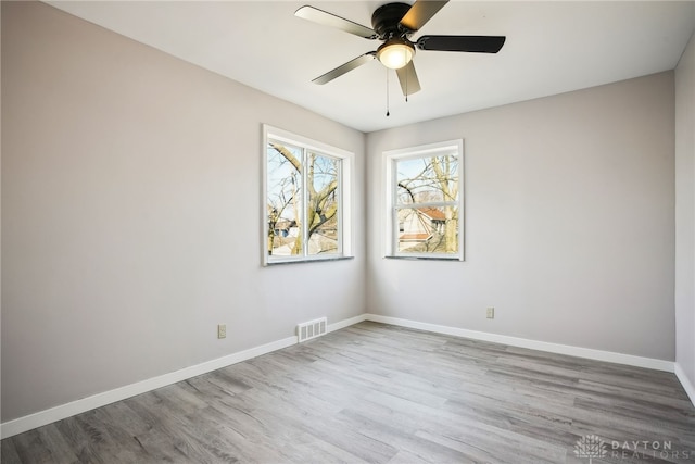 empty room with visible vents, a ceiling fan, baseboards, and wood finished floors