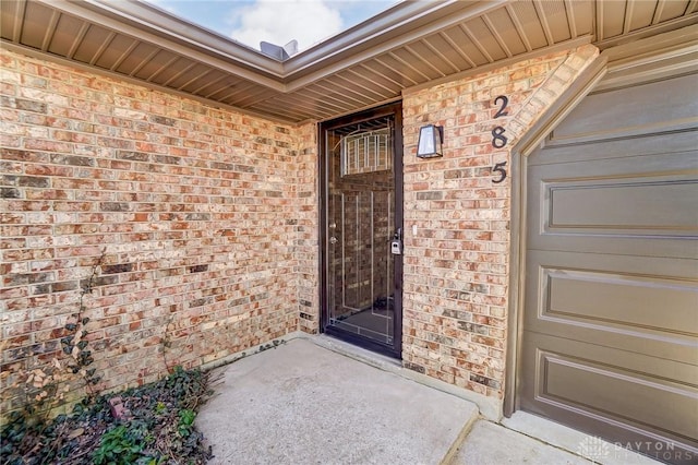 view of exterior entry featuring a garage and brick siding