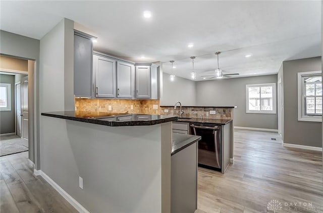 kitchen with tasteful backsplash, light wood-type flooring, gray cabinets, a peninsula, and stainless steel dishwasher