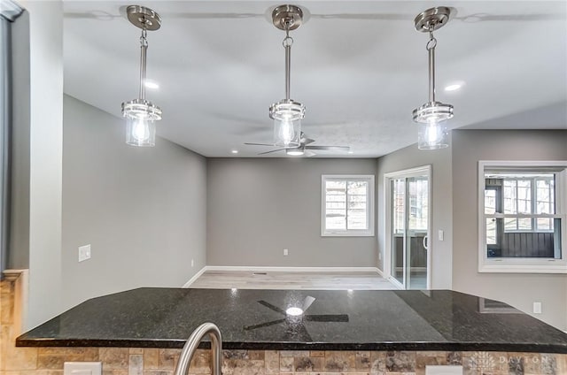 kitchen with hanging light fixtures, a healthy amount of sunlight, dark stone counters, and baseboards