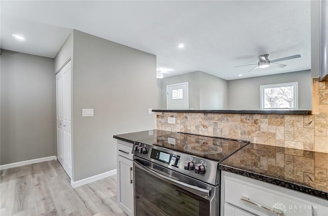 kitchen featuring light wood-type flooring, stainless steel range with electric stovetop, dark stone countertops, tasteful backsplash, and white cabinets