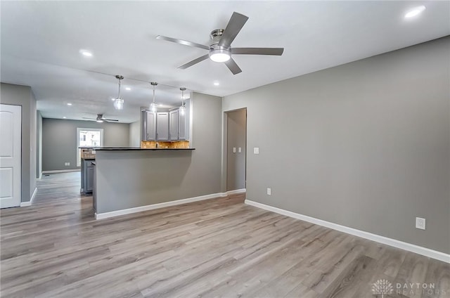 kitchen featuring light wood finished floors, dark countertops, baseboards, and decorative light fixtures