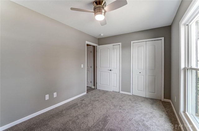 unfurnished bedroom with baseboards, multiple closets, carpet floors, and a ceiling fan