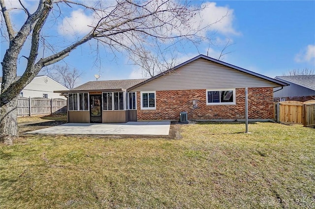 rear view of house with brick siding, a fenced backyard, a lawn, and a sunroom