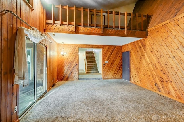 unfurnished living room featuring carpet flooring, wood walls, stairway, and a towering ceiling