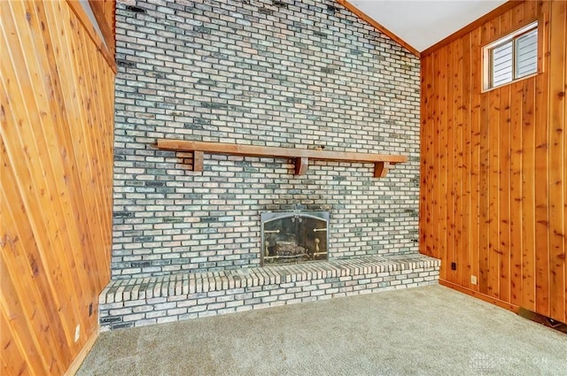 unfurnished living room with carpet floors, ornamental molding, vaulted ceiling, wood walls, and a brick fireplace