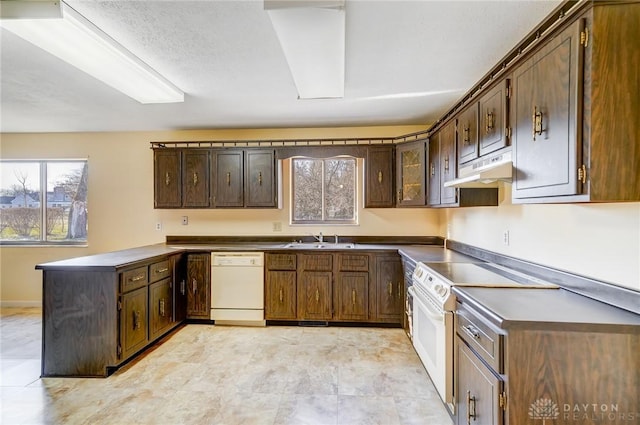 kitchen with dark countertops, under cabinet range hood, a peninsula, white appliances, and a sink