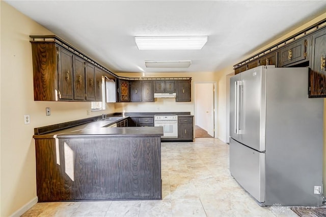 kitchen featuring oven, under cabinet range hood, dark brown cabinetry, a peninsula, and high quality fridge