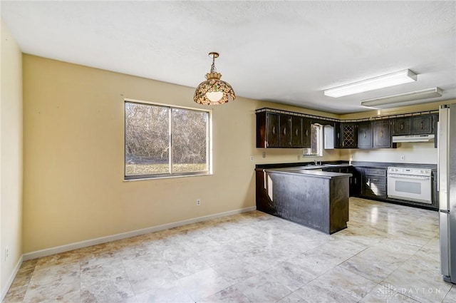 kitchen featuring baseboards, a peninsula, dark brown cabinets, under cabinet range hood, and white oven