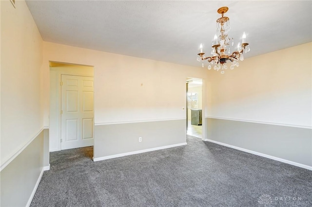 spare room with a notable chandelier, dark carpet, and baseboards