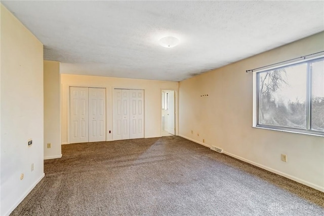 unfurnished bedroom with visible vents, carpet floors, baseboards, multiple closets, and a textured ceiling