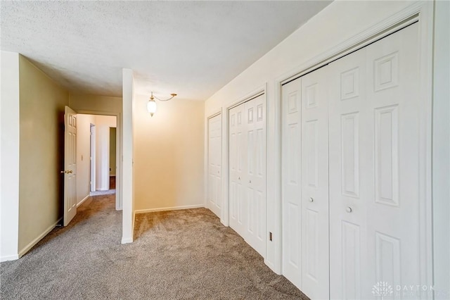 unfurnished bedroom featuring baseboards, multiple closets, a textured ceiling, and carpet flooring