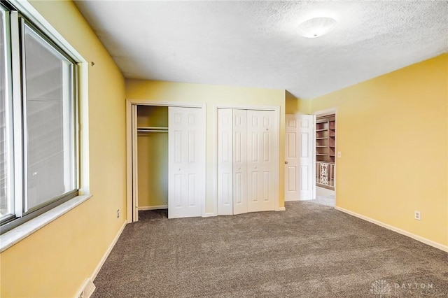 unfurnished bedroom with visible vents, two closets, a textured ceiling, carpet, and baseboards