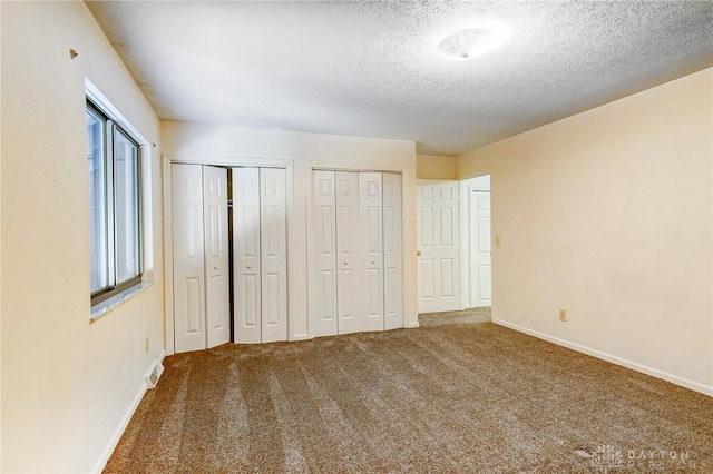 unfurnished bedroom featuring visible vents, multiple closets, a textured ceiling, carpet flooring, and baseboards