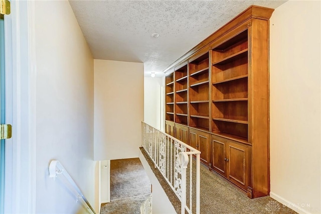 corridor with an upstairs landing, a textured ceiling, and carpet