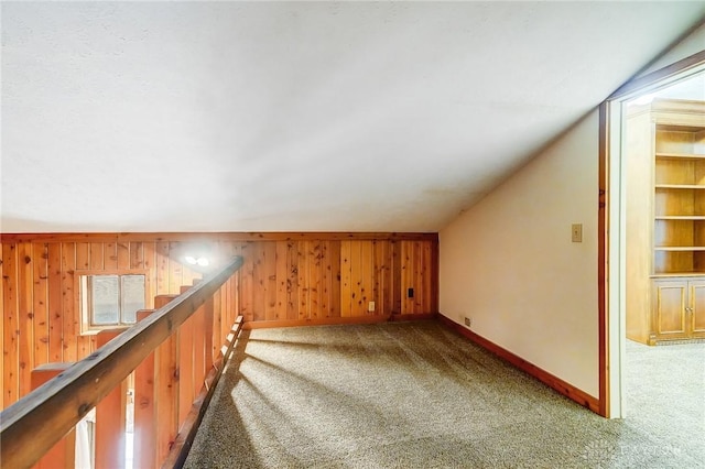 additional living space with wooden walls, baseboards, carpet, stairway, and vaulted ceiling