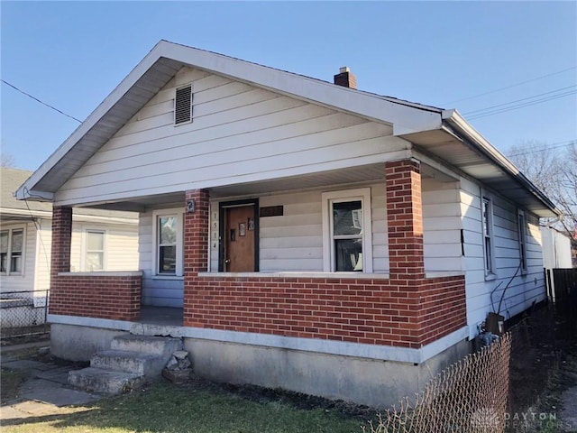 bungalow-style home with brick siding, covered porch, a chimney, and fence