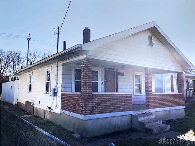 view of front of property featuring brick siding, a porch, and a chimney