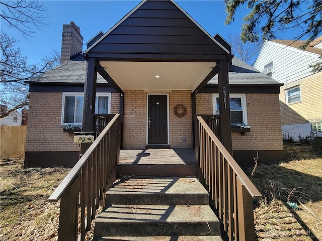 view of front of home with brick siding, a wooden deck, a chimney, and a shingled roof