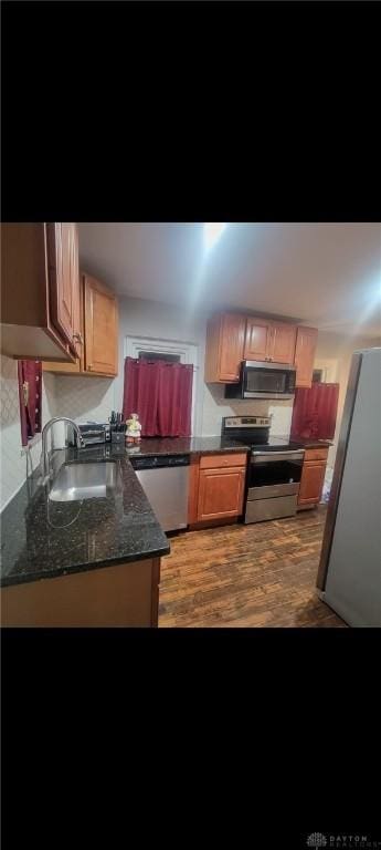 kitchen featuring a sink, stainless steel appliances, light wood-style flooring, and dark stone counters