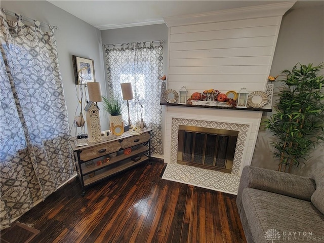 living area featuring a tiled fireplace, visible vents, and wood-type flooring