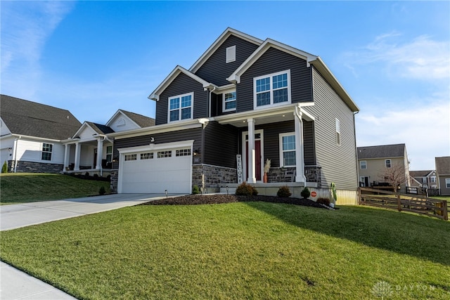 craftsman house with a front yard, fence, covered porch, concrete driveway, and stone siding