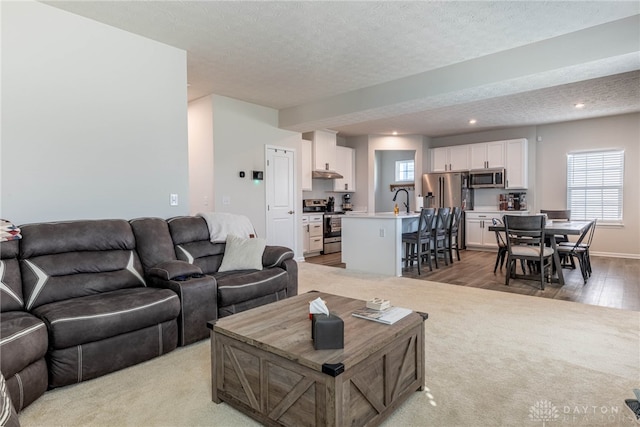 living area with recessed lighting, a textured ceiling, light wood-type flooring, and baseboards