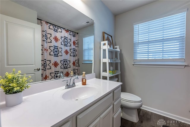 bathroom featuring vanity, toilet, visible vents, and a wealth of natural light