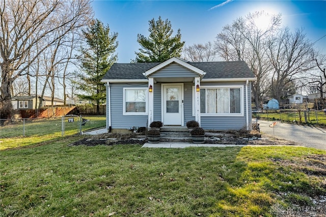 bungalow-style home with entry steps, a front lawn, fence, and roof with shingles