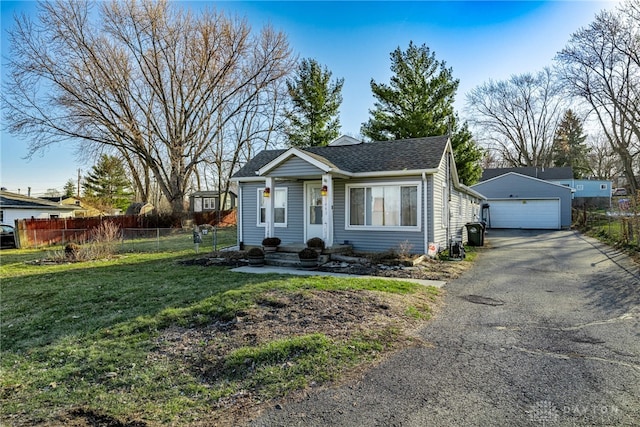 view of front of house with a shingled roof, a detached garage, a front lawn, fence, and an outdoor structure