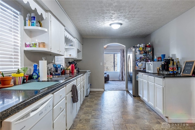 kitchen featuring dark countertops, open shelves, arched walkways, white appliances, and a sink