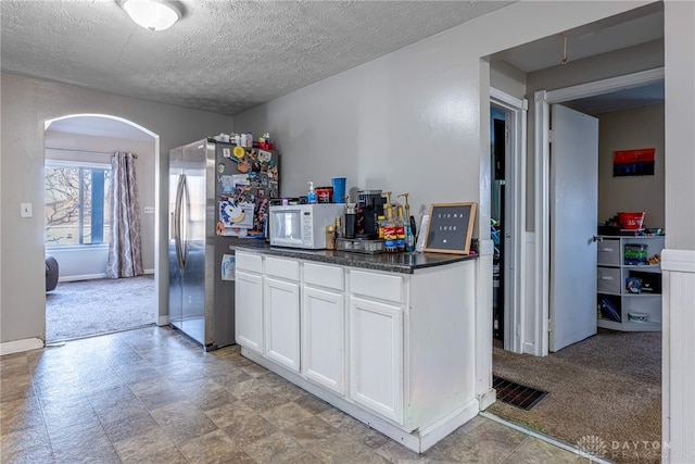 kitchen with white microwave, arched walkways, freestanding refrigerator, white cabinets, and light carpet