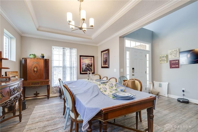 dining room featuring a chandelier, light wood finished floors, a tray ceiling, and ornamental molding