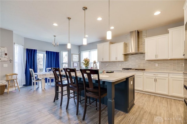 kitchen featuring a kitchen island, backsplash, wall chimney exhaust hood, light countertops, and a healthy amount of sunlight