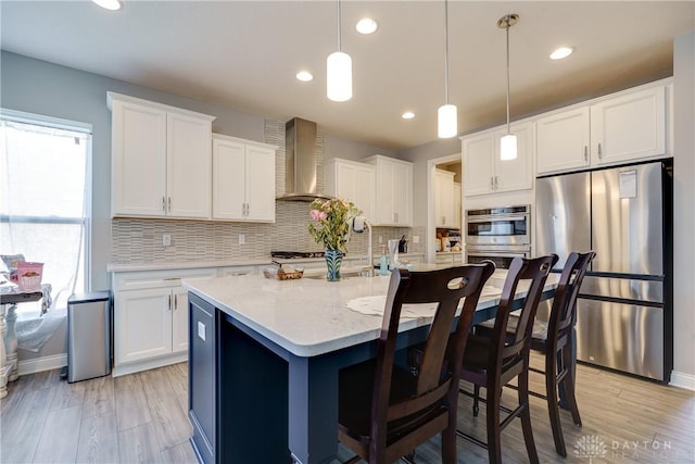 kitchen featuring backsplash, wall chimney range hood, pendant lighting, white cabinets, and stainless steel appliances