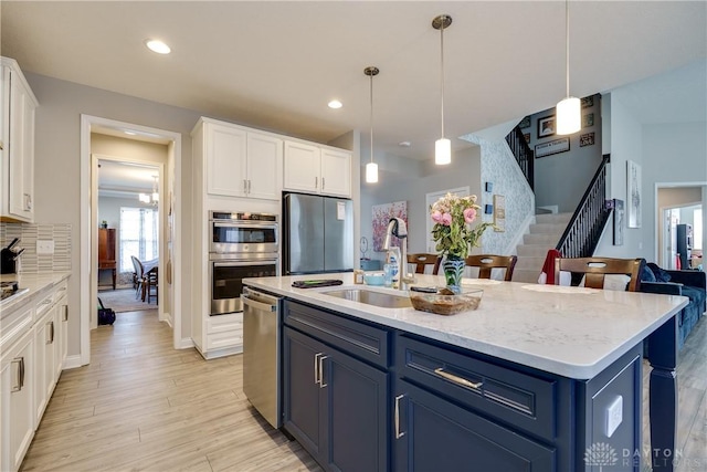 kitchen featuring light wood finished floors, appliances with stainless steel finishes, white cabinetry, and a sink