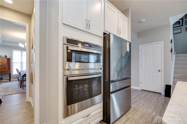 kitchen with baseboards, light stone counters, light wood-style flooring, stainless steel appliances, and white cabinetry