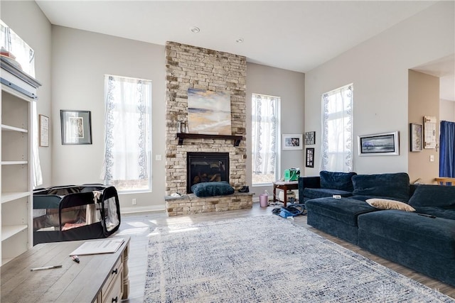 living area with baseboards, a stone fireplace, and wood finished floors