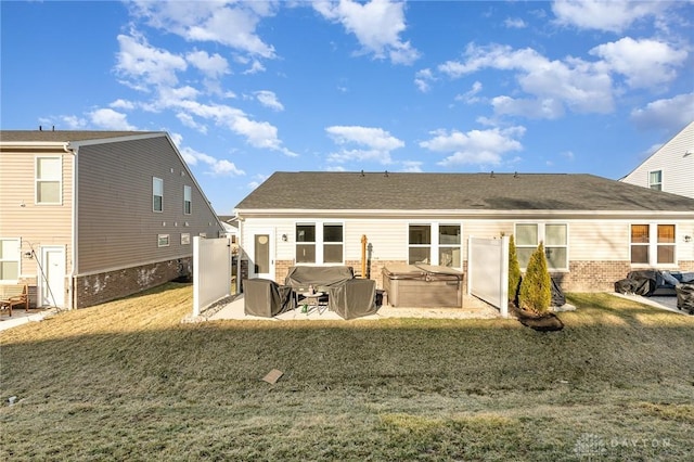 back of property featuring a yard, a patio area, brick siding, and a hot tub