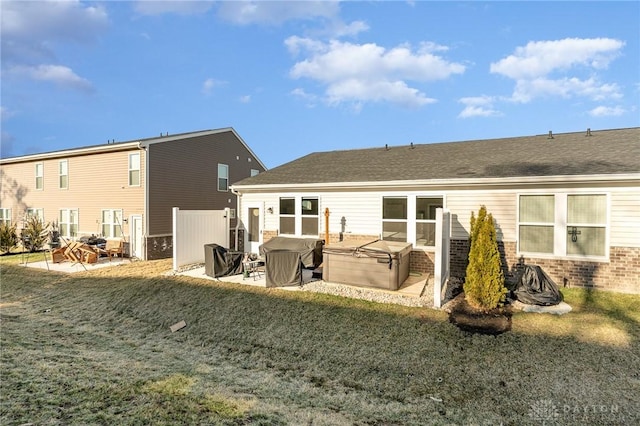 back of property with brick siding, a hot tub, a shingled roof, a lawn, and a patio area