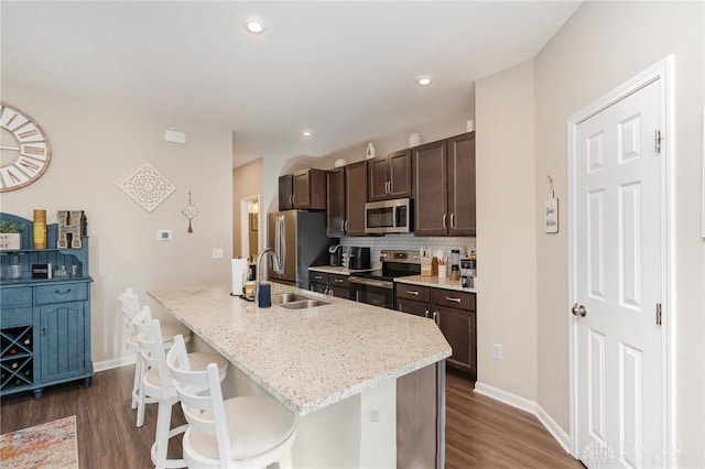 kitchen featuring a sink, decorative backsplash, stainless steel appliances, dark brown cabinets, and a kitchen breakfast bar