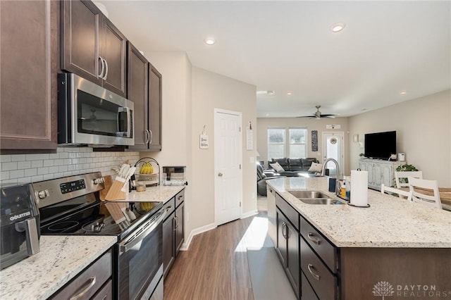 kitchen with an island with sink, a sink, stainless steel appliances, dark brown cabinetry, and backsplash