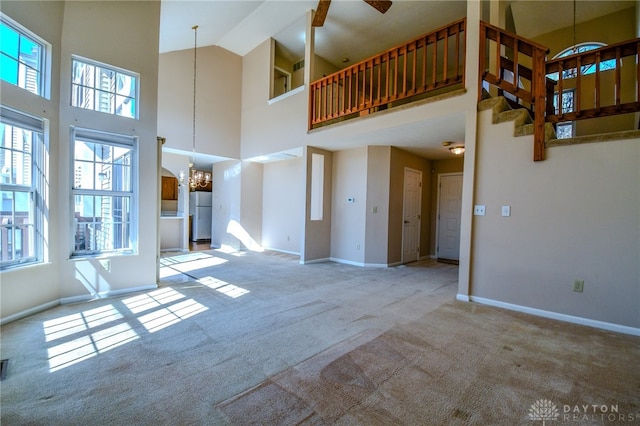 unfurnished living room with baseboards, carpet floors, a high ceiling, and ceiling fan with notable chandelier