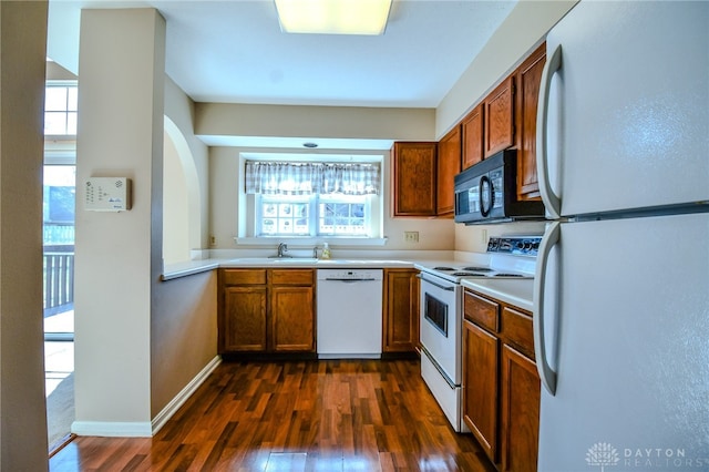 kitchen with brown cabinetry, white appliances, light countertops, and dark wood-type flooring