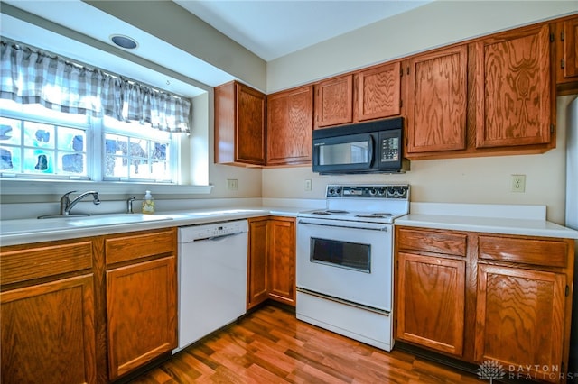 kitchen with white appliances, brown cabinetry, dark wood-style flooring, a sink, and light countertops