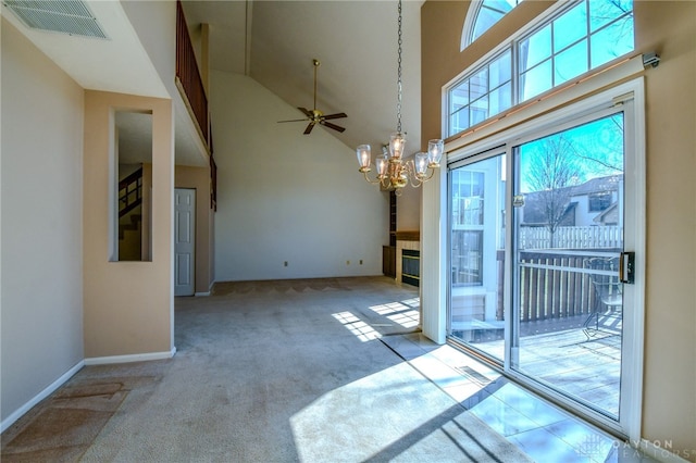 unfurnished dining area with visible vents, a tiled fireplace, carpet flooring, ceiling fan with notable chandelier, and high vaulted ceiling